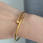 Тонкий браслет-цвях Cartier з камінням цирконію на кінцях з логотипом лимонне золото на руці
