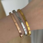 Тонкий жорсткий браслет Cartier з камінням та логотипом на руці