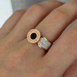 Широка каблучка BVLGARI з круглим логотипом та камінням золото чорний на руці