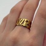 Широка каблучка Louis Vuitton з прорізами та логотипом лимонне золото на руці