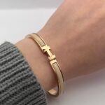 Вишуканий жорсткий браслет Hermes з логотипом у золоті бежевий на руці