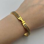 Вишуканий жорсткий браслет Hermes з логотипом у лимонному золоті бежевий на руці