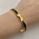 Вишуканий жорсткий браслет Hermes з логотипом у лимонному золоті чорний на руці